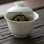 A minimalist white porcelain Gaiwan tea set on a dark wood tray.